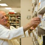 A pharmacist is selecting a drug from a display case in a pharmacy.