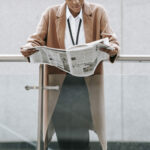 Crop black businesswoman reading newspaper near modern building