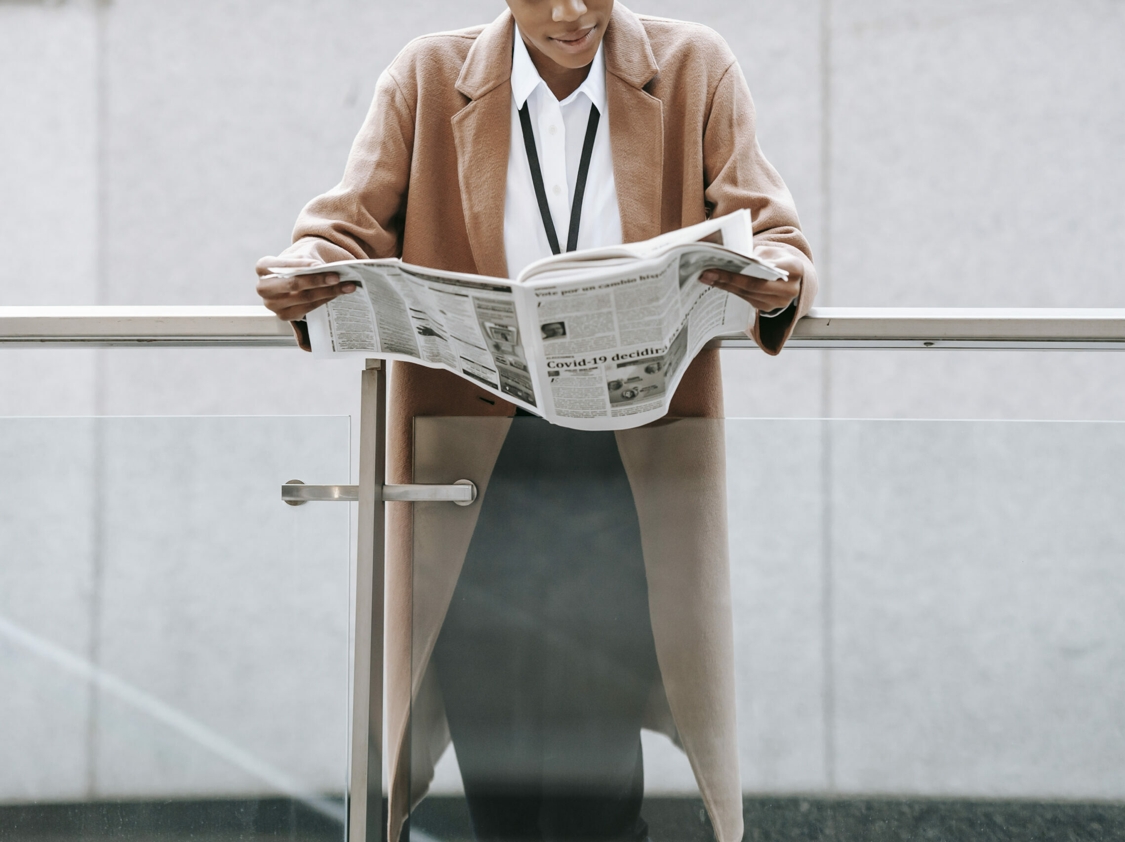 Crop black businesswoman reading newspaper near modern building