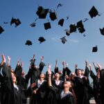 Newly graduated people wearing black academy gowns throwing hats up in the air