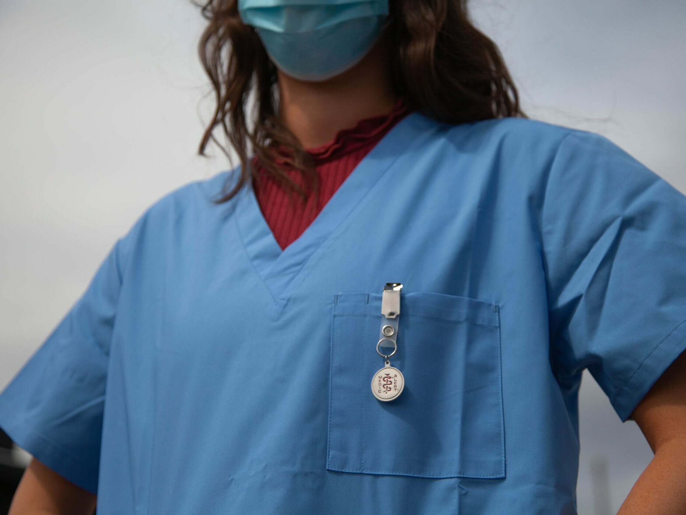 A nurse standing at the ready, wearing scrubs with a MedicAlert ID attached.
