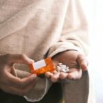 man's hand with pills spilled out of the container .