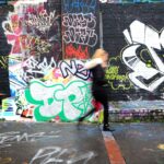 panning photography of woman walking beside wall with graffiti art