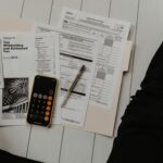 person holding paper near pen and calculator