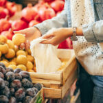 Female hands puts fruits and vegetables in cotton produce bag at food market. Reusable eco bag for shopping. Sustainable lifestyle. Eco friendly concept.