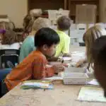 Captured in a metropolitan Atlanta, Georgia primary school, seated amongst his classmates, this photograph depicts a young Asian-American school boy, who was in the process of creating a drawing, and was choosing from a box of crayons, the colors he’d use in order to bring his ideas to life. It is important to know that these objects are known as fomites, and can act as transmitters of illnesses.