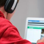 Home schooling during lockdown, boy working on school work with laptop and headphones during coronavirus covid 19 lock down. Remote learning through home schooling due to school closures has become commonplace in the UK in 2021.