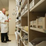 A male pharmacist is examining a drug from a the pharmacy inventory.