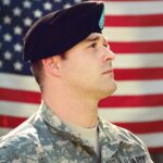 Man wearing combat hat and top looking up near flag of america