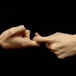 The hands of a young white person against a black background form the first half of the sign for “friendship” in American Sign Language.