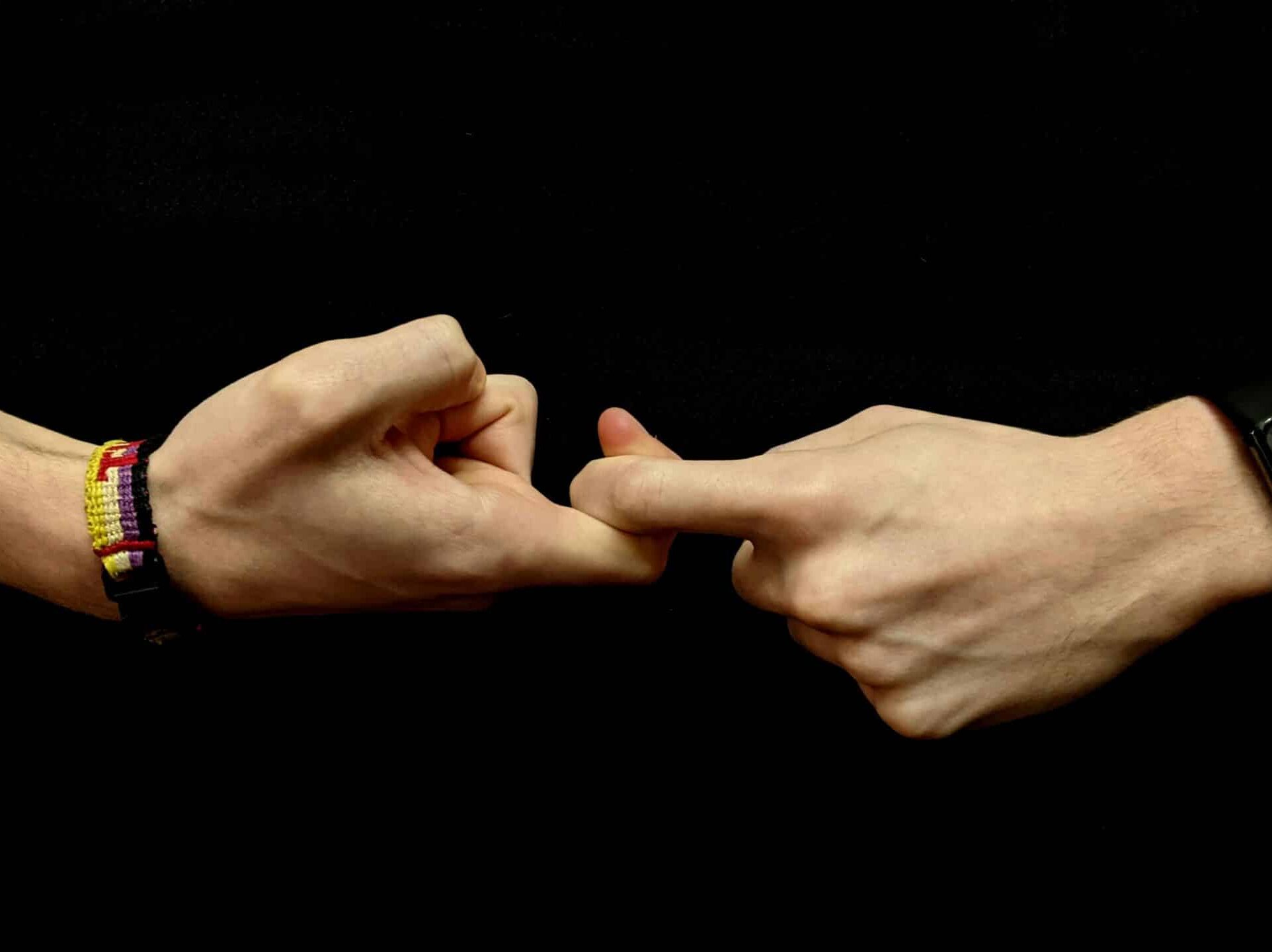 The hands of a young white person against a black background form the first half of the sign for “friendship” in American Sign Language.