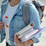 woman wearing blue denim jacket holding book