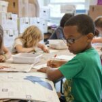 Captured in a metropolitan Atlanta, Georgia primary school, seated amongst his classmates, this photograph depicts a young African-American schoolboy who was in the process of drawing with a pencil on a piece of white paper. Note that the student was focused on a drawing book that referenced fantasy flying planes, while intent on creating his artwork, seemingly oblivious to all the classroom goings-on that surrounded him. It is important to know that objects, including pencils, crayons, paper, etc., are known as fomites, and can act as transmitters of illnesses.