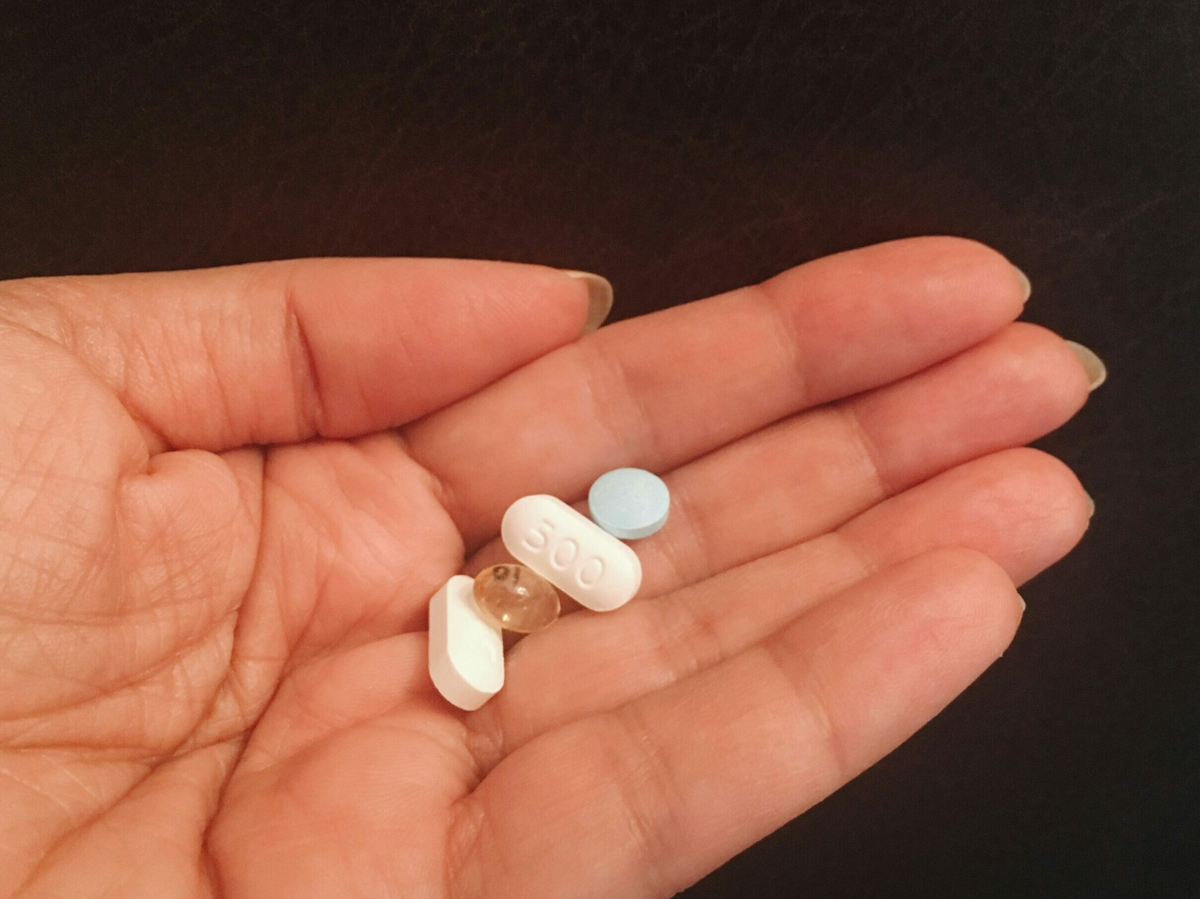 person holding four assorted medicine tablets