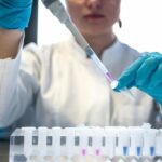 Female scientist pipetting colored chemicals into a tube.