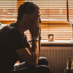 man sitting on chair covering his eyes