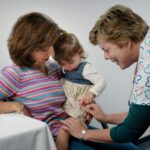 This photograph showed a young child being cradled by her mother, while she was receiving an intramuscular vaccination in her left thigh muscle. Notice that the nurse had immobilized the young girl's leg using her left hand.