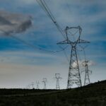 High tension power transmission pylons in front of a blue sky with clouds.