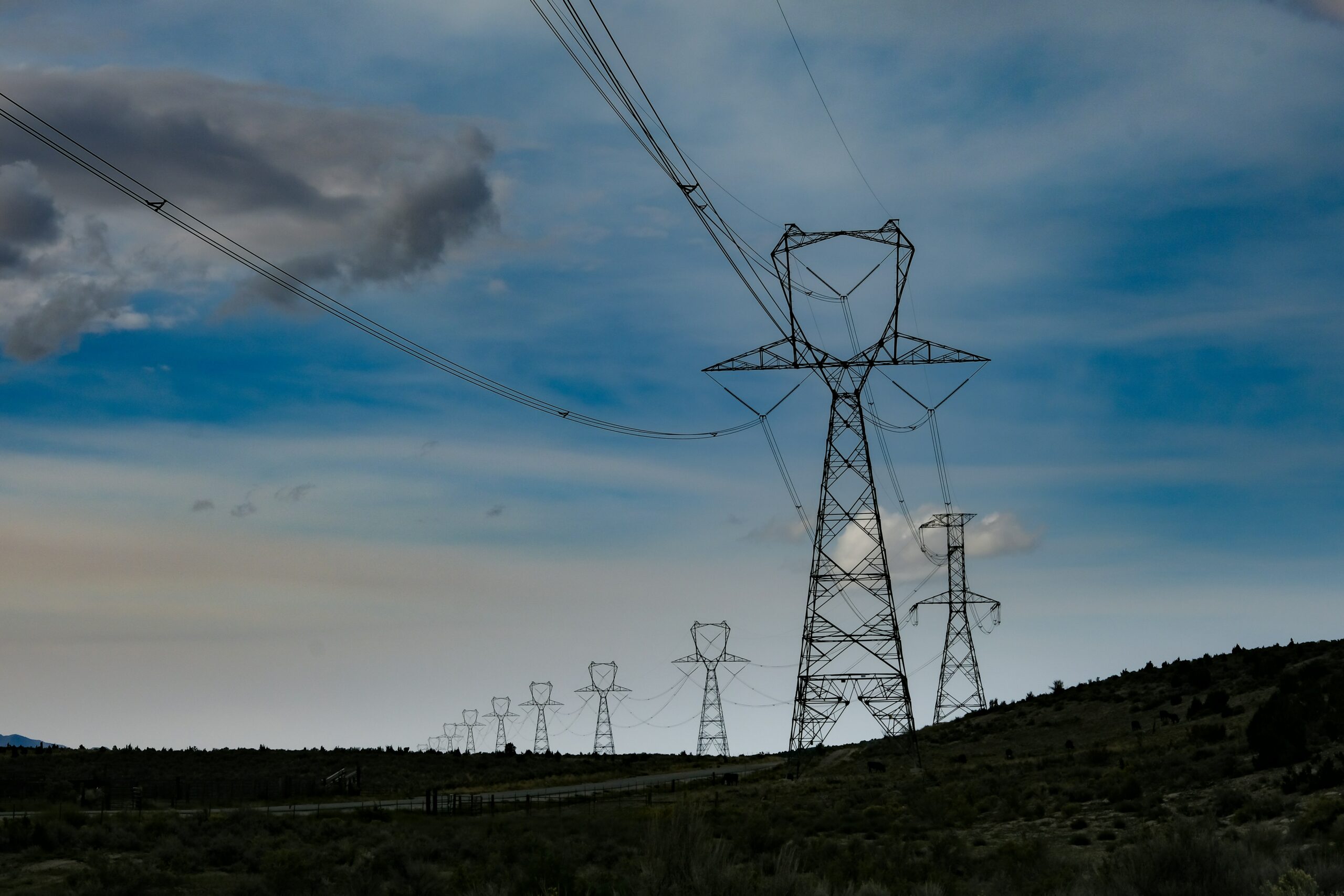 High tension power transmission pylons in front of a blue sky with clouds.