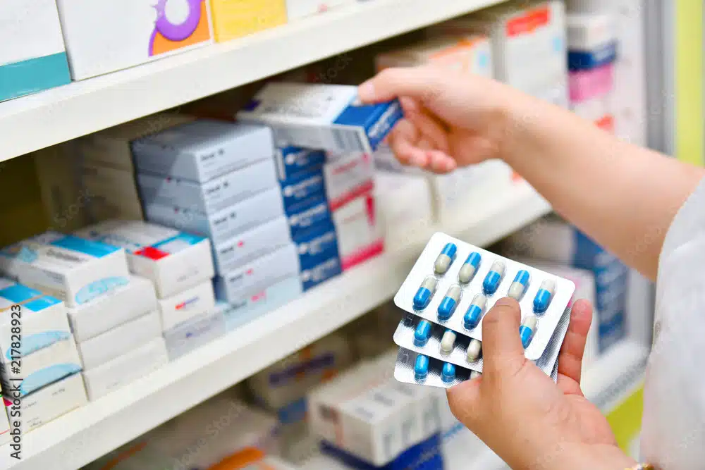 Pharmacist holding medicine box and capsule pack in pharmacy drugstore.