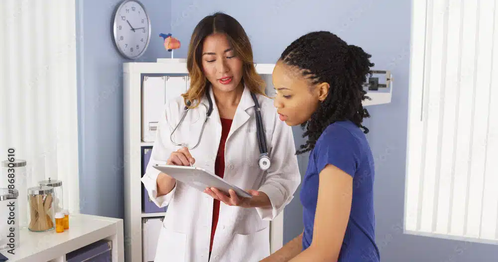 African American patient explaining issues to Asian doctor using tablet